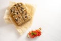 Low carb protein bread with seeds on baking paper and a tomato sandwich with parsley garnish on a white table, healthy slimming