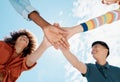 A low close up view of a group of diverse young friends joining hands in a huddle while smiling with a blue sky in the Royalty Free Stock Photo