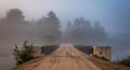 Low cloud and darkened skies. Single point perspective, surreal coloured subdued light from summer storm over single lane bridge.