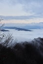 Low clouds, view of winter forest and mountains from observation deck, vertical picture of amazing natural phenomenon. Beautiful