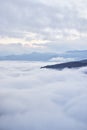 Low clouds, view of winter forest and mountains from observation deck, vertical picture of amazing natural phenomenon. Beautiful