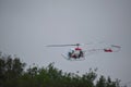 Low flying helicopter chopper just over the trees tops on a cloudy day with pilot visible