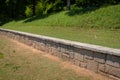 Low granite block retaining wall in an urban park, green grass and trees