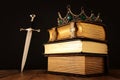 low key image of beautiful queen/king crown over antique book and sword. fantasy medieval period. Selective focus Royalty Free Stock Photo