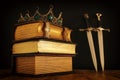 low key image of beautiful queen/king crown over antique book and sword. fantasy medieval period. Selective focus Royalty Free Stock Photo