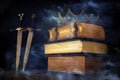 low key image of beautiful queen/king crown over antique book and sword. fantasy medieval period. Selective focus. mist and fog