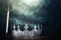 low key image of beautiful queen or king crown over antique next to sword. fantasy medieval period. Selective focus. Glitter Royalty Free Stock Photo