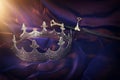 Low key image of beautiful queen/king crown and sword over dark royal purple delicate silk. fantasy medieval period