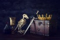 low key image of beautiful queen/king crown, wine cup, bird skeleton and sword. fantasy medieval period.