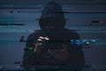 Low-key image of a hooded hacker typing on a smartphone, with digital code and glitch overlays suggesting cybercrime, data theft, Royalty Free Stock Photo