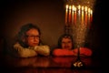 Low key image of jewish holiday Hanukkah background with two cute kids looking at menorah traditional candelabra