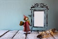 Low key image of old victorian steel blue blank frame, tree log with fairy lights and cute fairy on wooden table