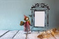 Low key image of old victorian steel blue blank frame, tree log with fairy lights and cute fairy on wooden table