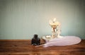 Low key image of white Feather, inkwell, and candle on old wooden table.