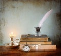 Low key image of white Feather, inkwell and candle on old wooden table. image textured.
