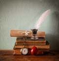 Low key image of white Feather, inkwell, scroll ancient books on old wooden table