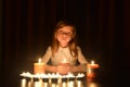 The cute little blonde girl holds a burning candle. Lots of candles are around her, over dark background Royalty Free Stock Photo