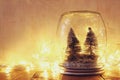 Low key and vintage filtered image of christmas trees in mason jar with garland warm lights and glitter overlay. selective focus