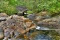 Low, mid-summer woodland creek and waterfall along rock boulders and under the arched bridge. Royalty Free Stock Photo