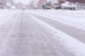 A low portrait of an asphalt road or street covered in snow and ice during winter. There are frozen tire tracks visible in the