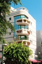 A low-rise building with a bright facade, large glass windows and large balconies with interesting plants that wrap around them.