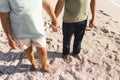 Low section of active senior multiracial couple holding hands while standing on sand at sunny beach Royalty Free Stock Photo