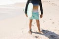 Low section of biracial senior man holding surfboard standing on shore at sunny beach Royalty Free Stock Photo