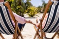 Low section of caucasian romantic senior couple holding hands and sitting on deck chairs at beach