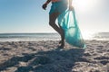 Low section of man carrying plastic bag with waste walking at beach on sunny day Royalty Free Stock Photo