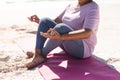 Low section of senior biracial woman meditating in lotus position at beach on sunny day Royalty Free Stock Photo