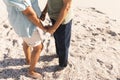 Low section of senior multiracial couple holding hands while standing on sand at sunny beach Royalty Free Stock Photo