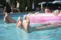 Low section of two friends in a pool holding onto an inflatable raft with feet sticking out of the water