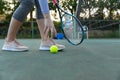 Low section of woman holding tennis racket picking up ball on outdoor tennis court, with copy space Royalty Free Stock Photo