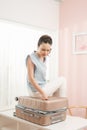 Low section of woman kneeling on overstuffed suitcase on bright room Royalty Free Stock Photo