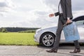 Low section of young businessman with gas can walking by broken down car at countryside