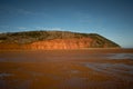 Sand bar off at low tide showing beautiful red sand cliff face with trees and blue sky Royalty Free Stock Photo