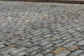 Low view of a gray stone block street seen from an oblique angle, transportation background with selective focus