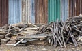 Low view, piles of logs of different sizes are piled on the ground near old galvanized walls