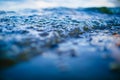 Low wave bubbles reaching coastline macro. Water texture