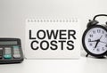 lOWER COSTS words with calculator and clock with notebook