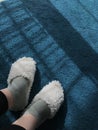 the lower part of the legs in white slippers on a blue carpet on the floor Royalty Free Stock Photo