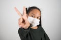 Lttle girl with medical mask show v sign with hand, healthcare and infection control. Concept of positivism against the infection Royalty Free Stock Photo