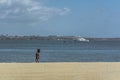 View at the beach on Mussulo Island, with a man walking, water with a boat and jets, on Luanda city and the sky as background Royalty Free Stock Photo