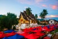 Famous night market in Luang Prabang, Laos with illuminated temple and sunset sky