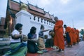 luangprabang lao-july20,2023 : lao monk receiving sticky rice and food from asian woman on luangprabang street against beautiful