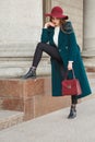 Lucky fashion girl. In hat with large fields, long warm coat, a white sweater and a lady`s leather purse.