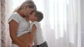 Lucky kid embraces future mother with big belly in room in natural light