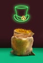 Lucky treasure minimal concept. Bag full of golden coins. Green Neon sign of top hat with yellow fluorescent cloves buckle. Plum Royalty Free Stock Photo