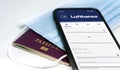 Lufthansa airlines mobile app on the screen lying over a protective mask and a passport Royalty Free Stock Photo