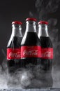 Lugansk, Ukraine - July 25, 2021: Coca Cola in glass bottles with water drops condensate and frozen smoke on dark